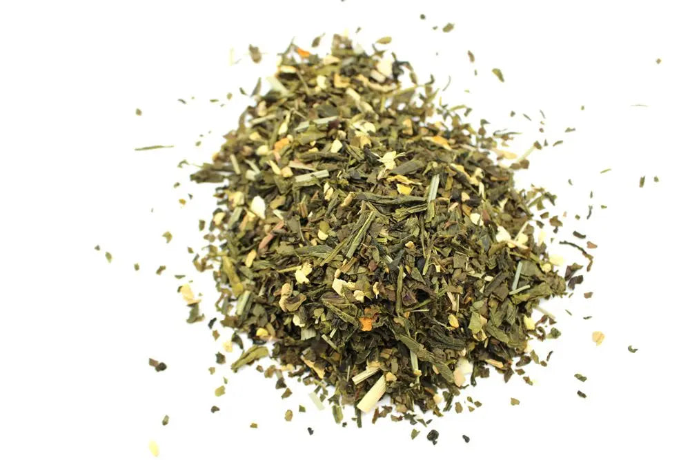 Montón de té verde seco mezclado con trozos de jengibre y piel de limón sobre fondo blanco.