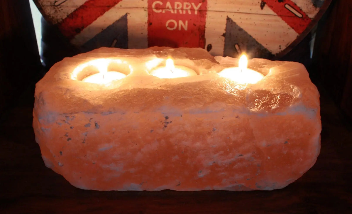 Portavelas rectangular de sal del Himalaya, color naranja, con tres velas encendidas en su interior. Textura rugosa.