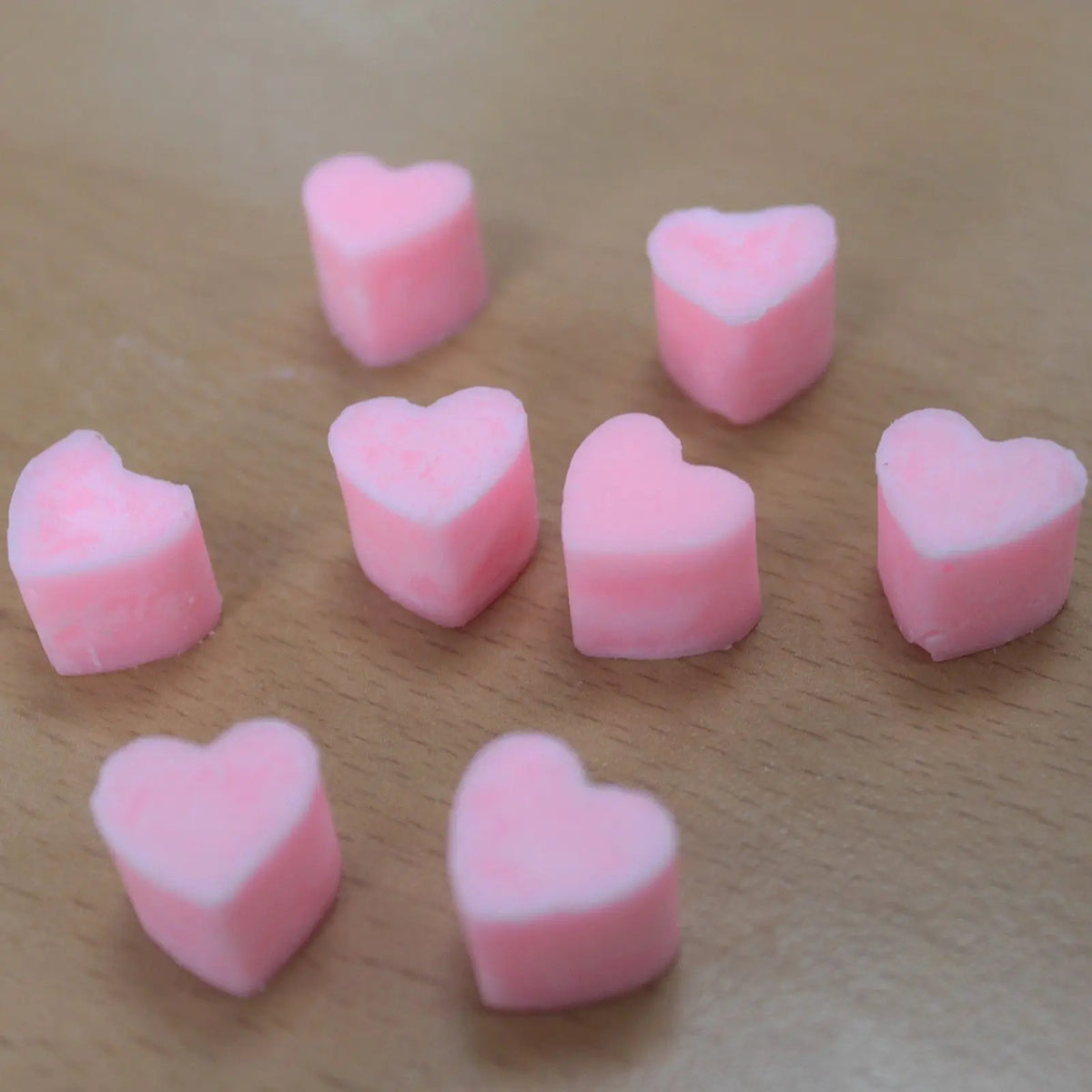 Ocho corazones de cera rosa dispersos sobre una superficie de madera clara.