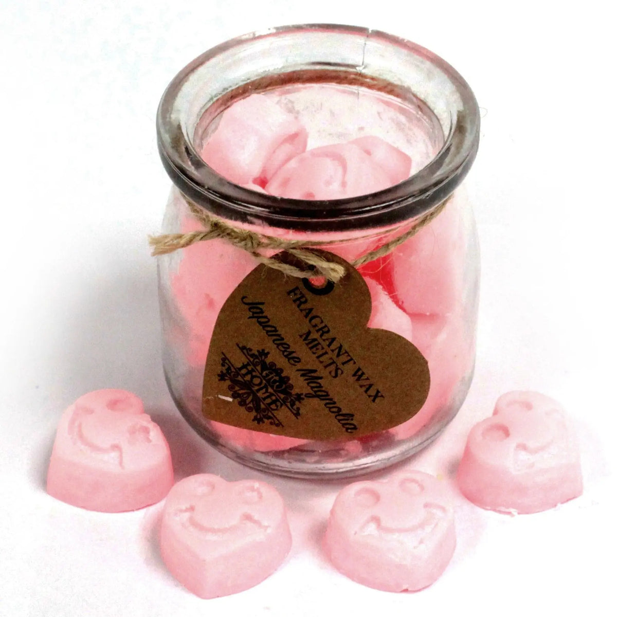Frasco de vidrio con cera de soja rosa en forma de caritas sonrientes, decorado con una etiqueta en forma de corazón.