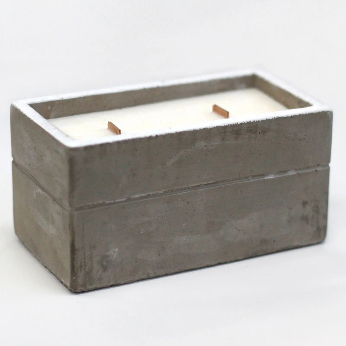 Vela rectangular de cera blanca con dos mechas de madera en un recipiente de hormigón gris con estilo rústico moderno.