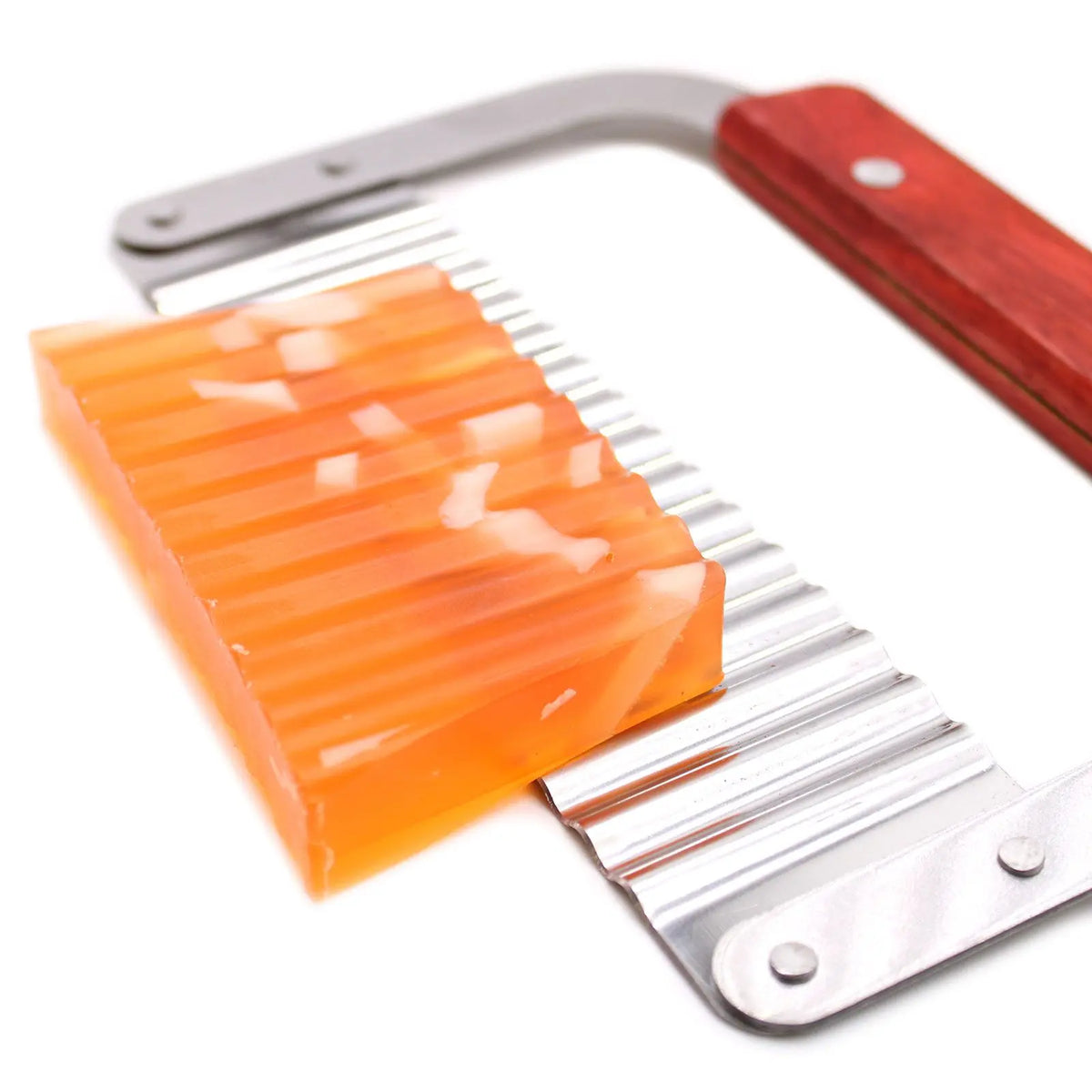 Cortador de jabón ondulado de metal con mango de madera, cortando una barra de jabón naranja translúcido.