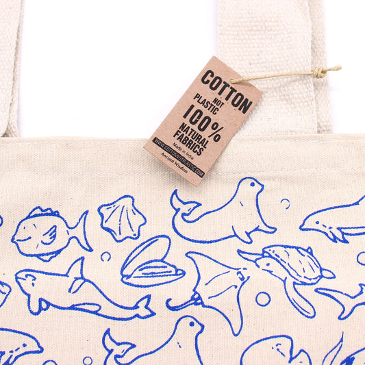 Bolsa de algodón crudo con estampado azul de fauna marina y etiqueta de cartón informativa colgando.