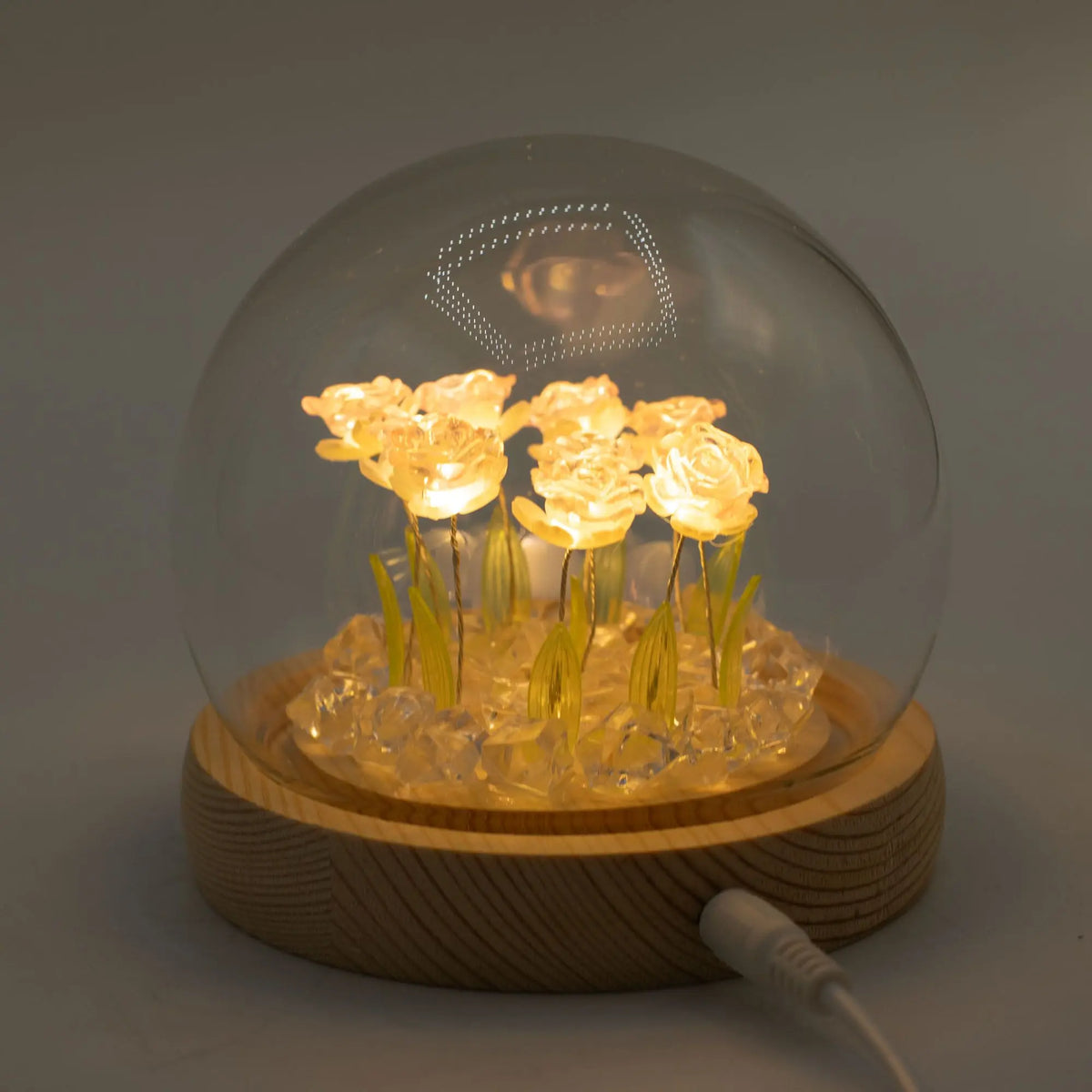 Domo de cristal con 10 rosas brillantes LED sobre base de madera circular. Iluminación cálida, diseño elegante.