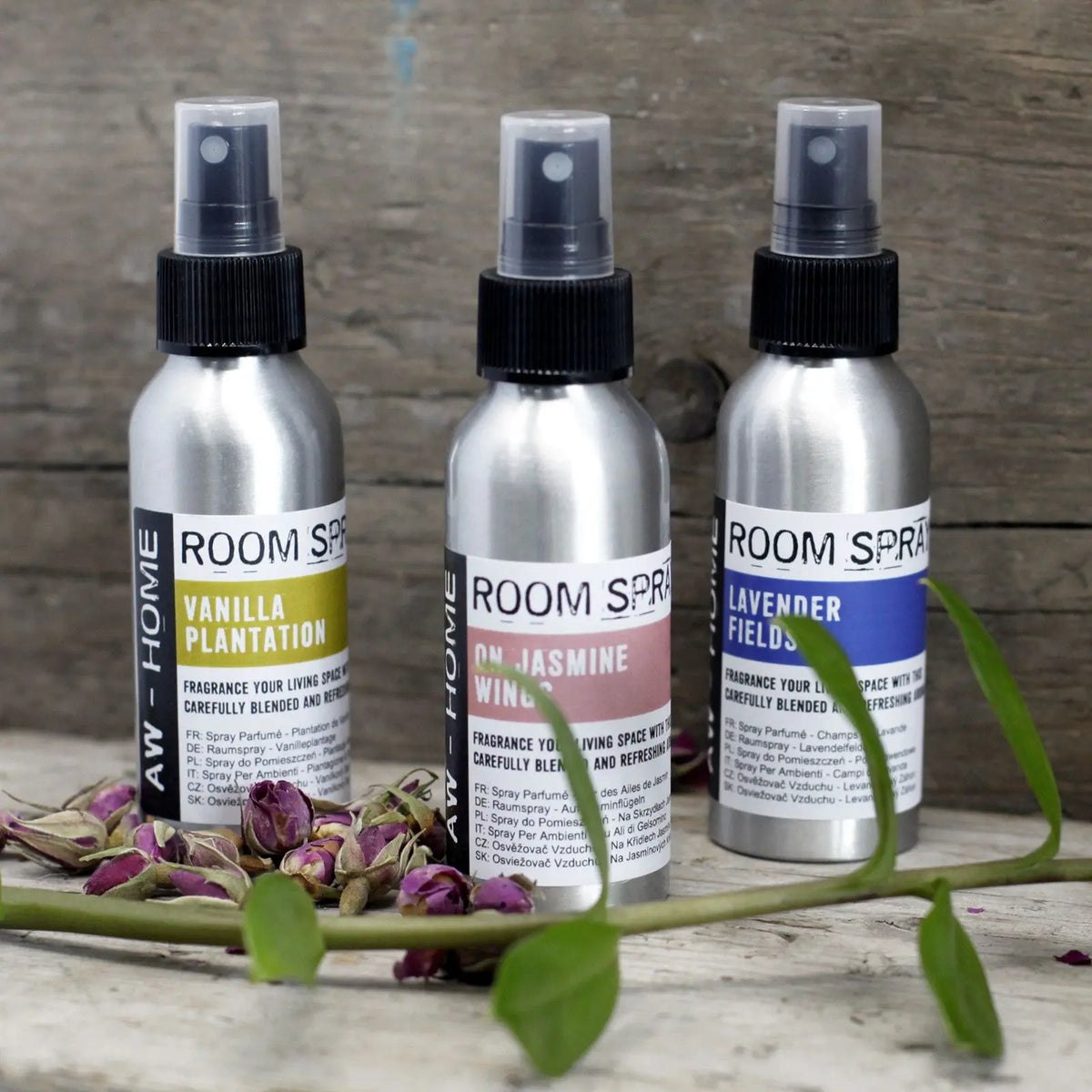 Tres sprays de 100ml en envases de aluminio con atomizador negro, sobre superficie de madera con pétalos y ramas.