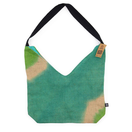 Bolso de hombro de yute verde azulado con manchas claras, corte en V y asa larga negra. Etiqueta de cartón colgando.