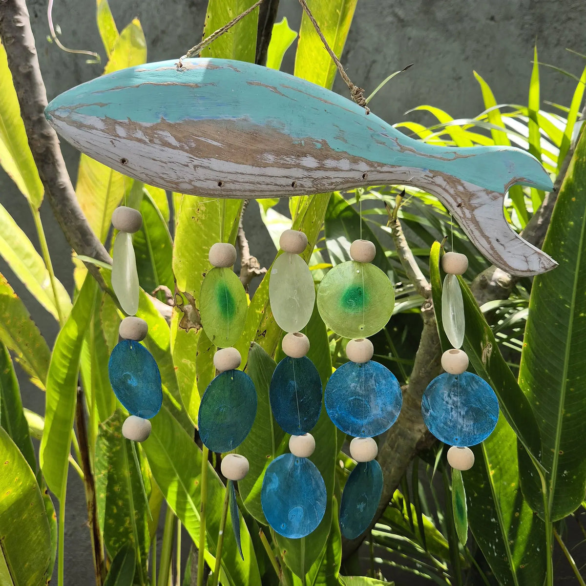 Carillón de madera con forma de pez en azul y blanco, con colgantes de cuentas de madera y discos de nácar en tonos aqua.