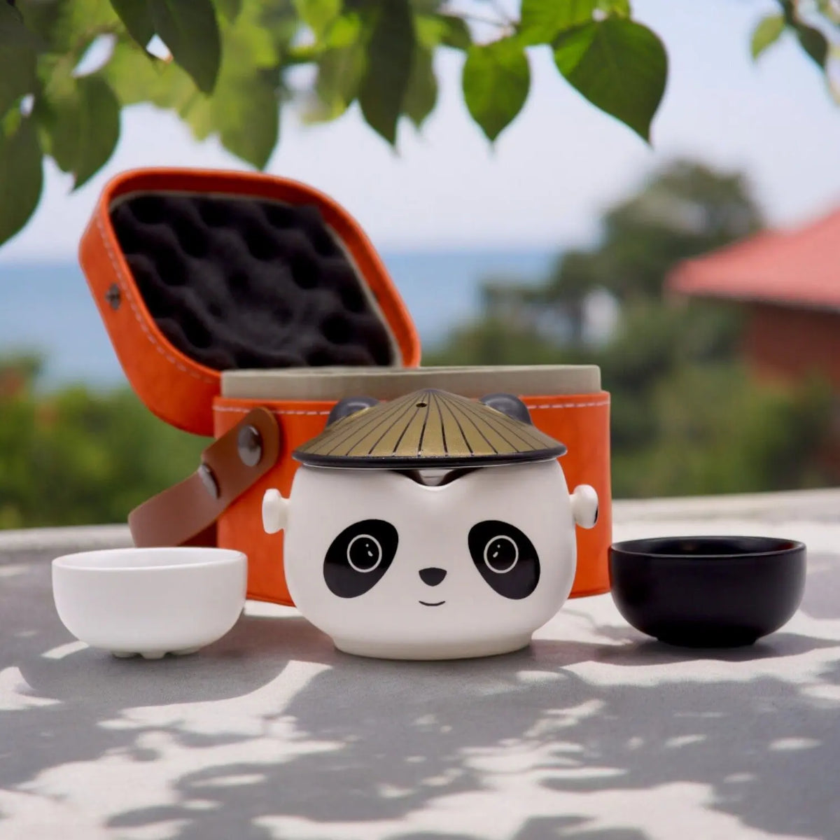 Set de té con tetera cerámica diseño panda, dos tazas, una blanca y una negra, y estuche de viaje naranja protector