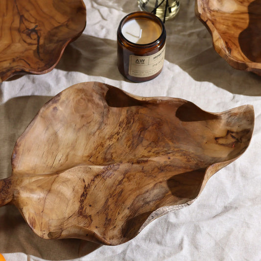 Frutero de madera de teca en forma de hoja, con vetas naturales y tonos marrones, sobre un mantel de lino claro.