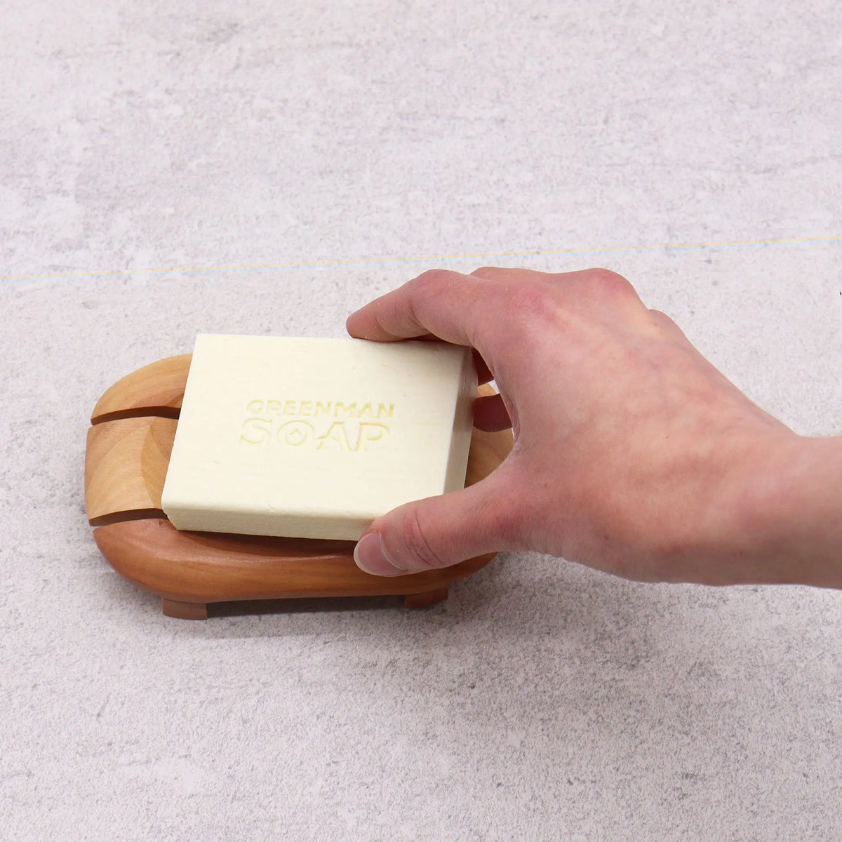 Jabonera ovalada de caoba Ancient Wisdom sobre superficie clara, con mano sosteniendo pastilla de jabón beige.