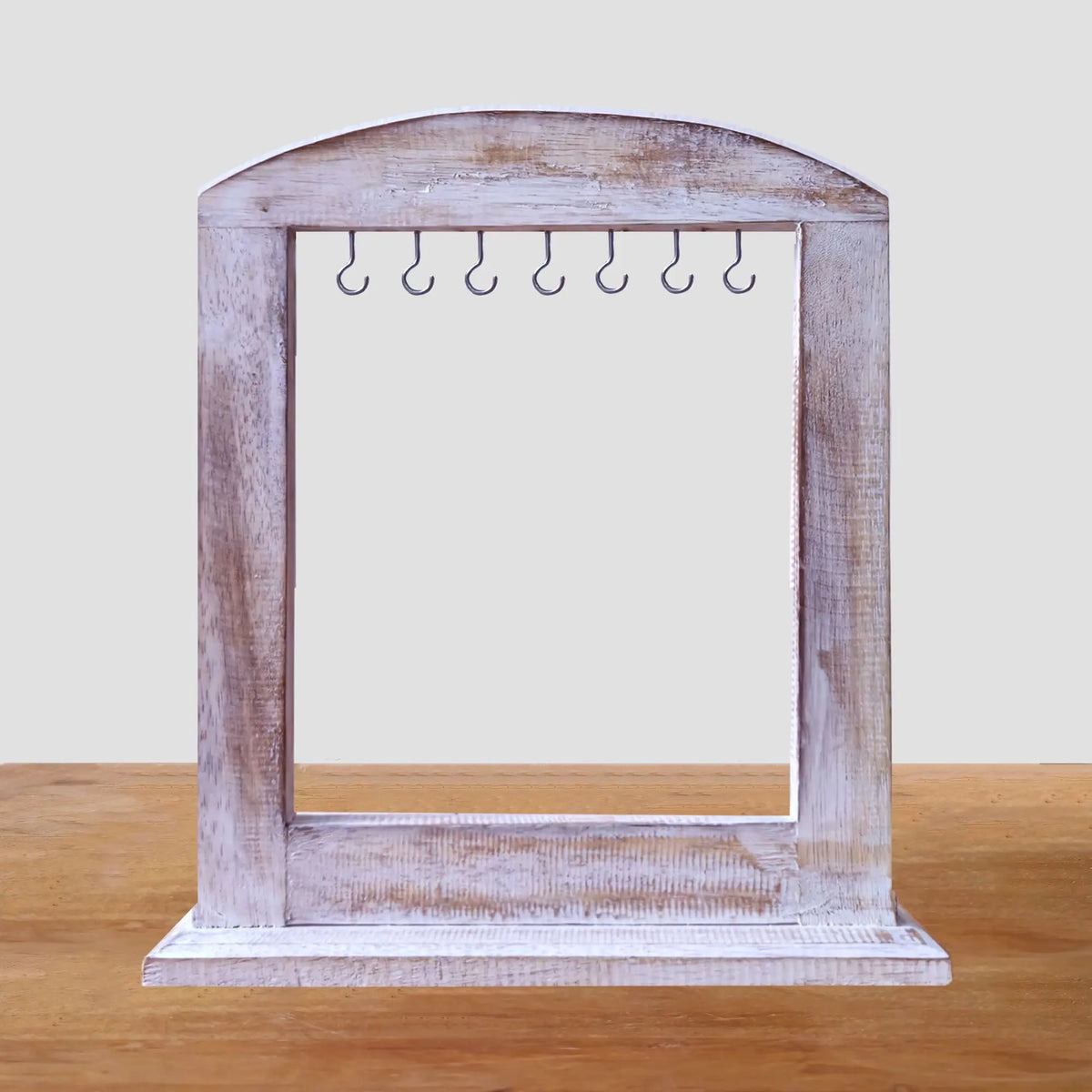 Soporte de madera blanqueada con forma de arco y ganchos metálicos superiores para exhibir artículos artesanales.