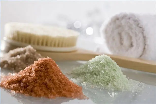 Montículos de sales de baño aromáticas de colores, un cepillo de madera y una toalla blanca enrollada en un spa.