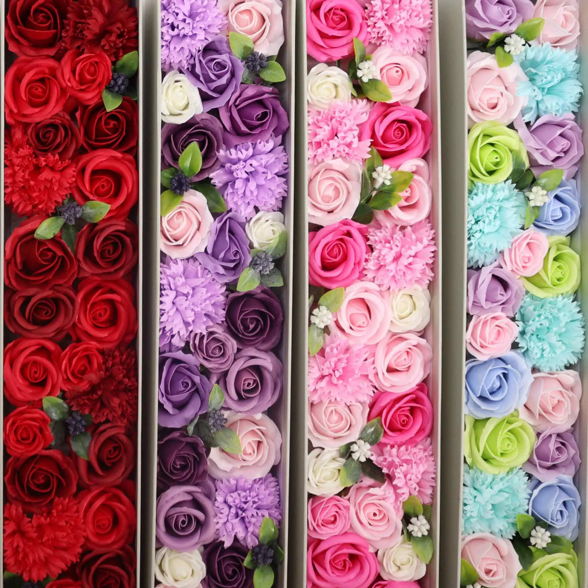 Cajas alargadas con rosas y claveles de jabón en diversos colores, decoradas con pequeñas hojas verdes.