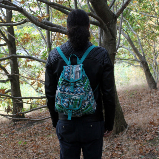 Mochila de tejido jacquard con estampado geométrico en tonos verde azulado, blanco y negro sobre fondo de bosque.