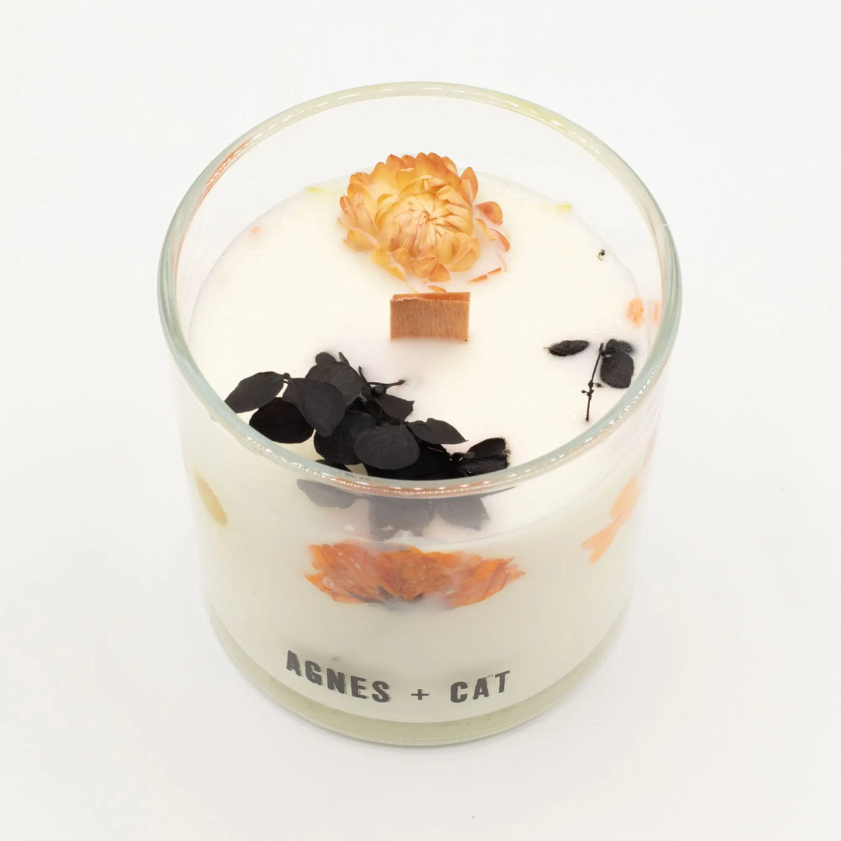Vela aromática blanca con flores secas naranjas y negro, en frasco de vidrio, estilo elegante y moderno.