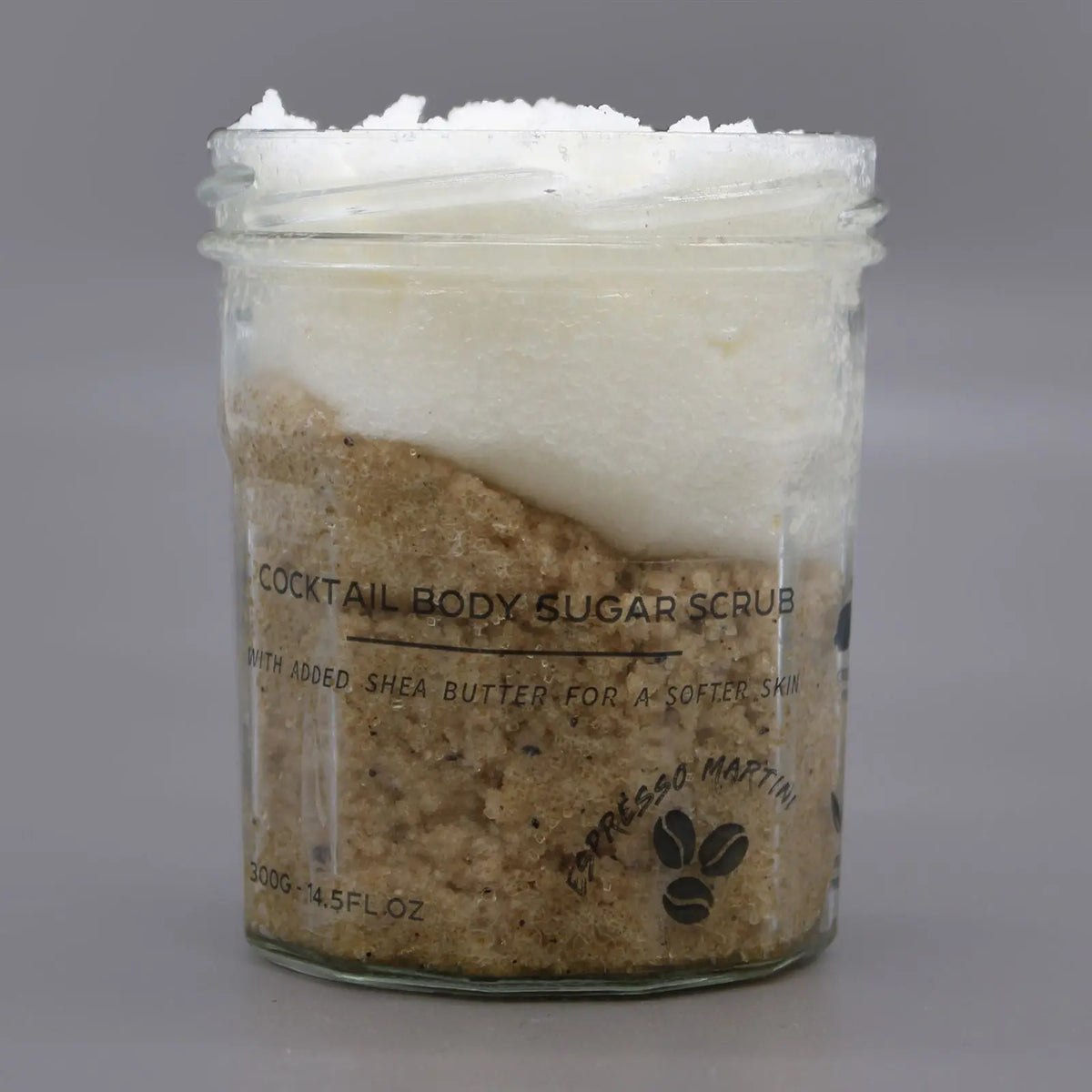 Exfoliante corporal en frasco de vidrio con capas de azúcar blanca y café, diseño minimalista sobre fondo gris claro