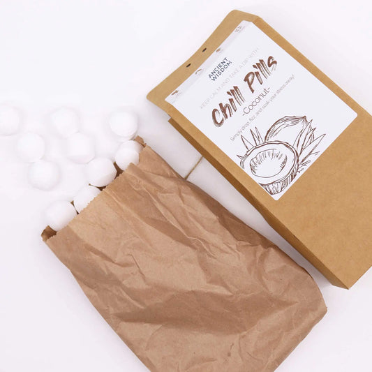 Mini bombas de baño blancas esféricas saliendo de una bolsa de papel kraft junto a su caja de cartón con etiqueta.