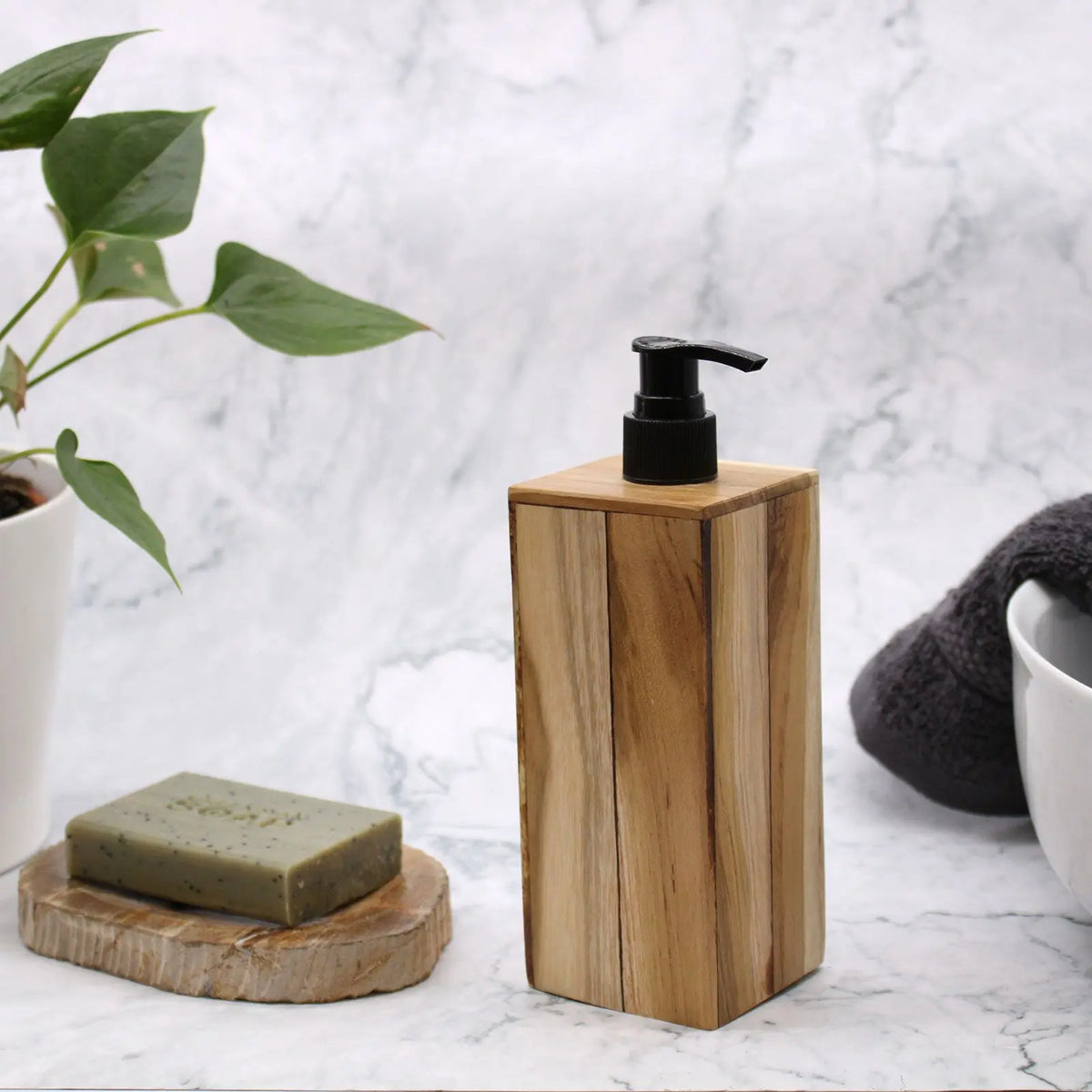 Dispensador de jabón cuadrado de madera de teca natural con dosificador negro sobre fondo de mármol.