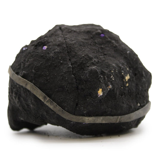 Mineral negro con brillo metálico y detalles morados, decorado con una banda de metal plateado, estilo moderno.