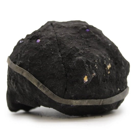 Mineral negro con brillo metálico y detalles morados, decorado con una banda de metal plateado, estilo moderno.