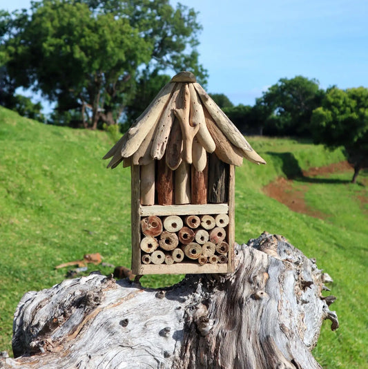 Refugio para insectos hecho de madera y troncos, con techo a dos aguas y celdas tubulares en un entorno natural.