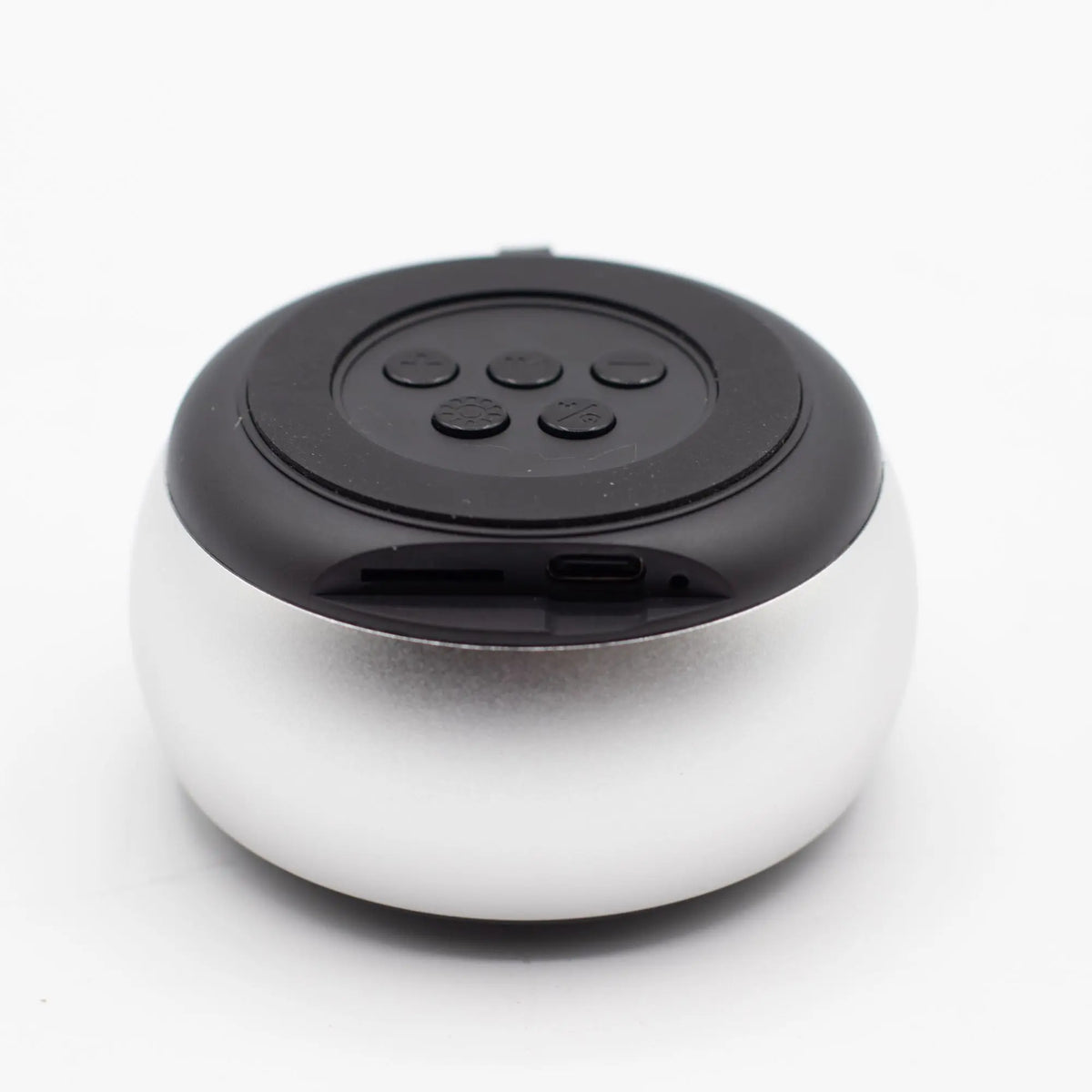 Altavoz Bluetooth mini, forma redonda plateada con parte superior negra, botones de control y puertos de carga.