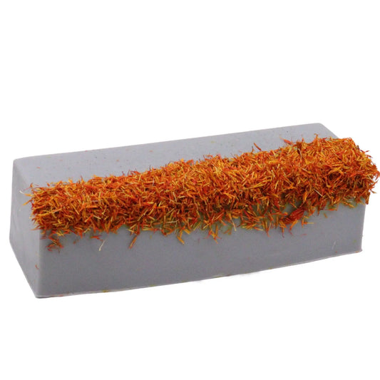 Barra de jabón rectangular gris decorada con una franja superior de pétalos secos de color naranja y amarillo.