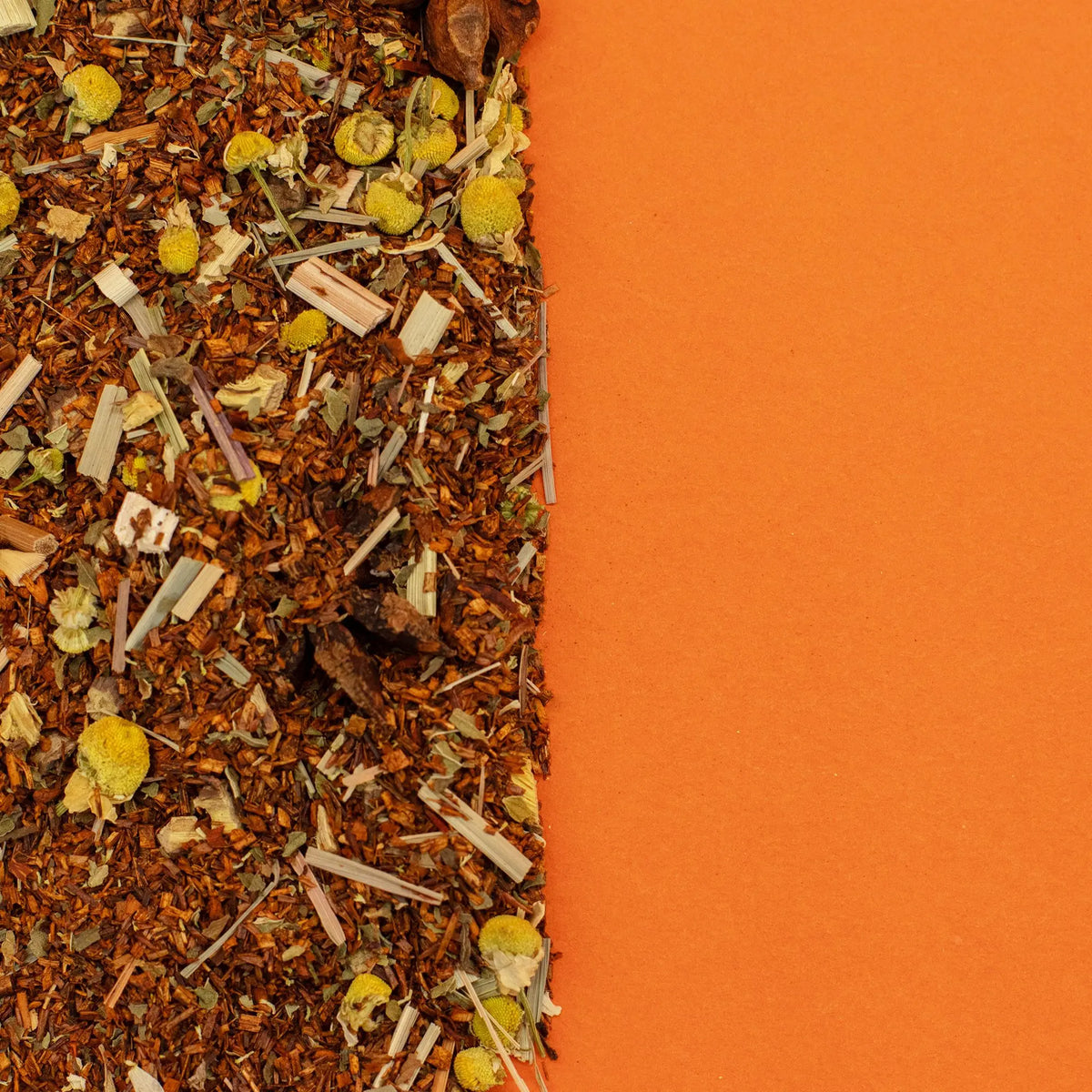 Mezcla de té rooibos con flores de manzanilla y hierbas sobre un fondo naranja sólido.