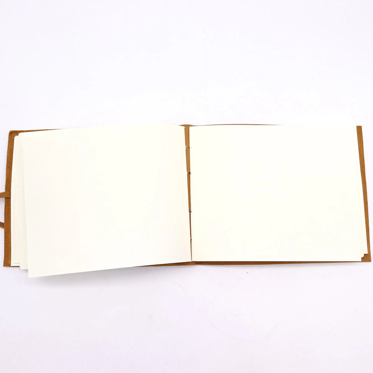 Cuaderno de viaje abierto con cubierta de cuero marrón y hojas de papel crema en blanco sobre fondo blanco.