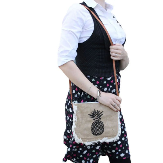 Bolso bandolera de yute color natural con flecos y estampado de piña negra, colgado al hombro.