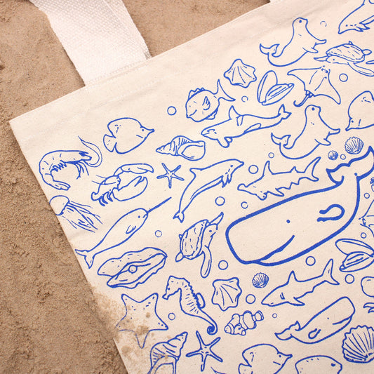 Bolsa de algodón color crema con estampado azul de vida marina, sobre fondo de arena. 38x42cm.