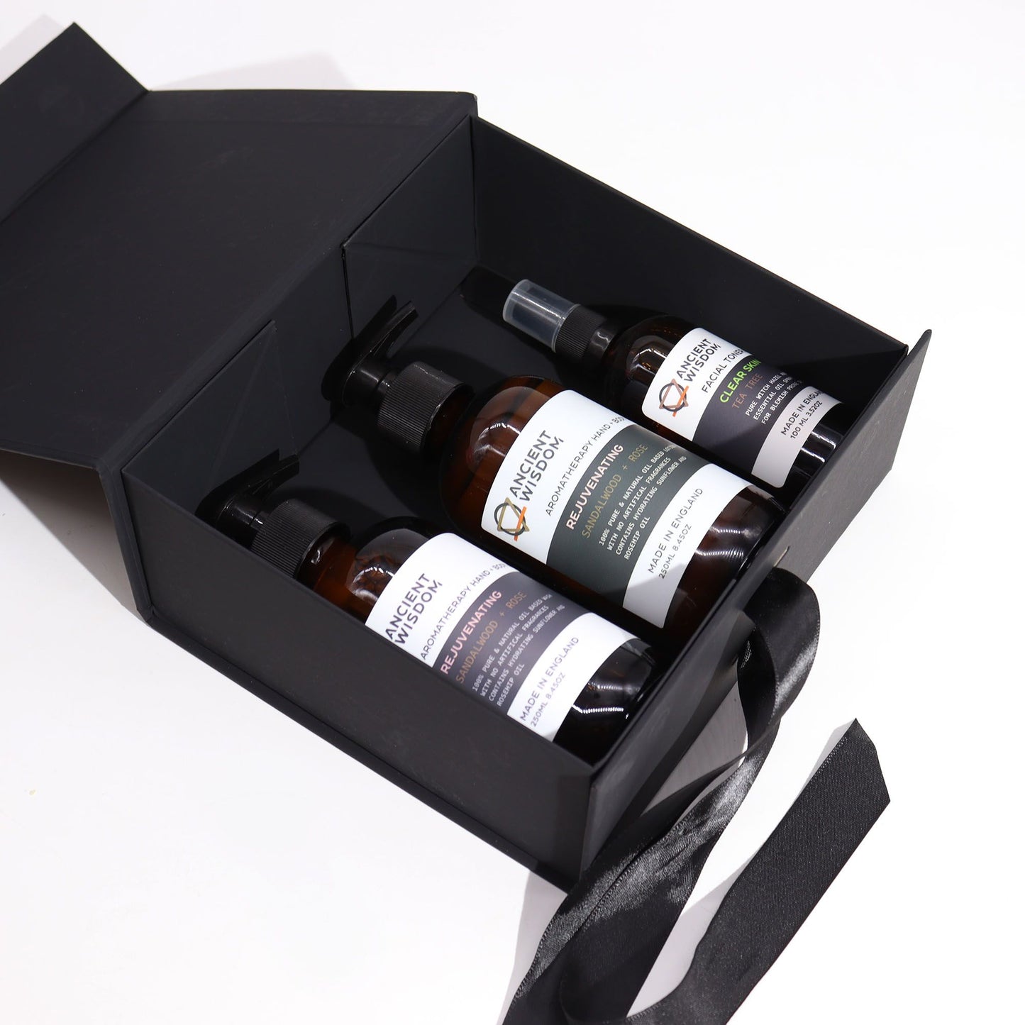 Caja de regalo negra plegable con lazo que contiene tres frascos de productos de cuidado personal sobre fondo blanco