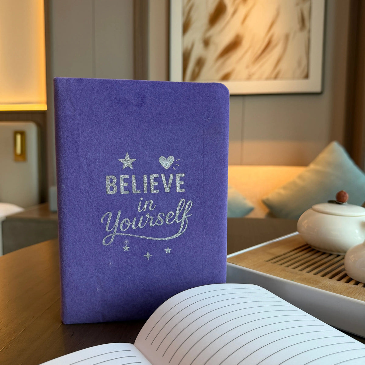 Cuaderno de terciopelo morado con la frase "Believe in Yourself" en letras plateadas y diseño de estrellas y corazón.