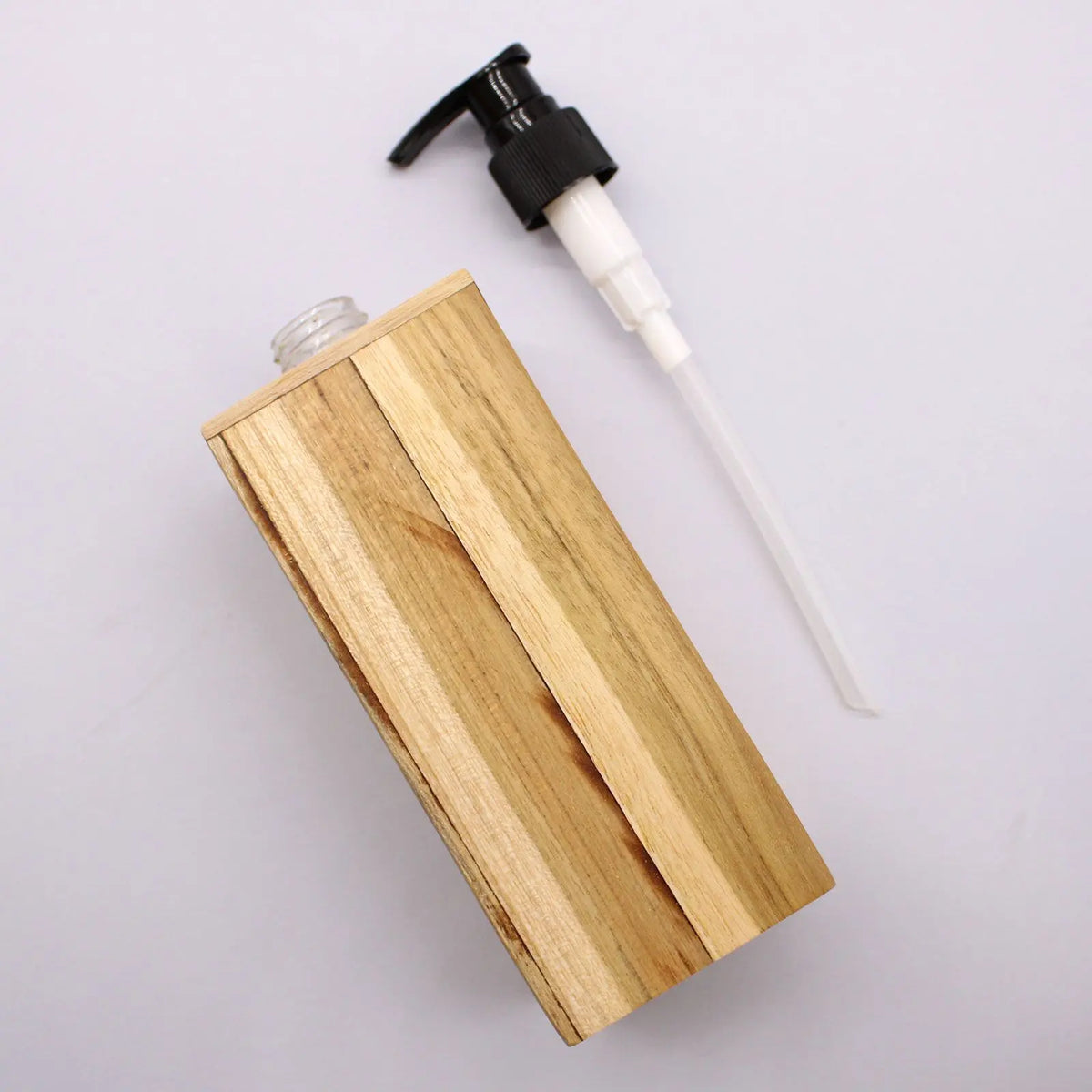 Dispensador de jabón cuadrado de madera natural con bomba dosificadora negra y blanca sobre fondo gris claro.