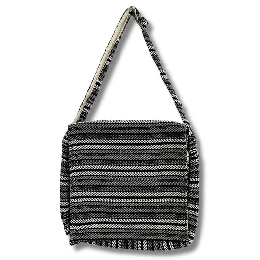 Bolso de tela rectangular con patrón de rayas grises y negras, estilo artesanal y correa larga para el hombro.