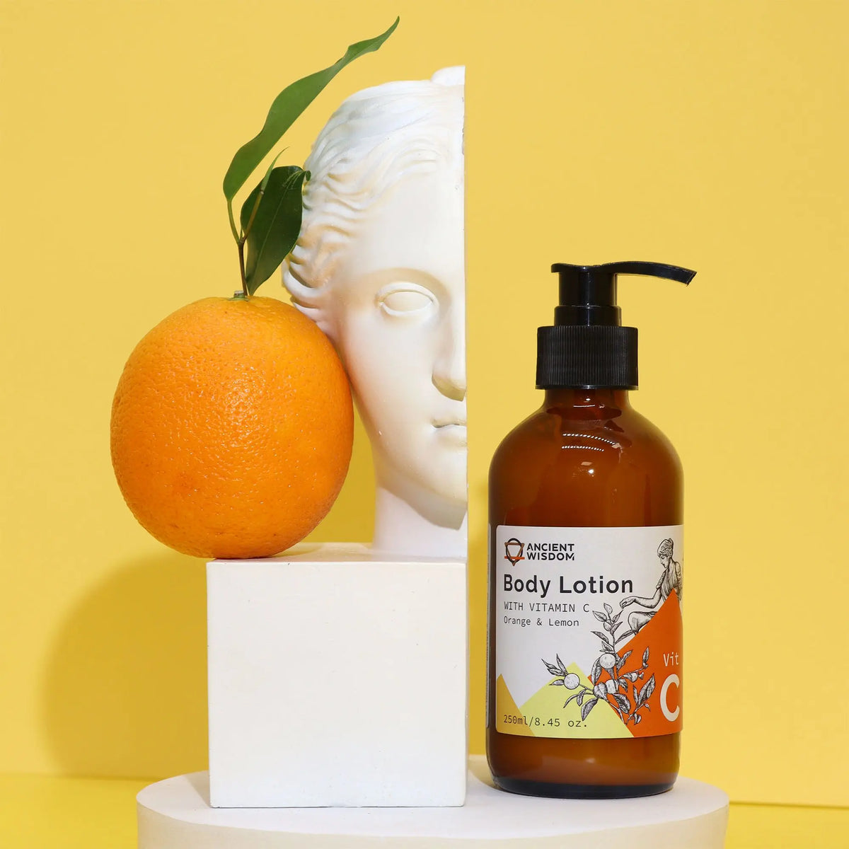 Loción Vitamina C Ancient Wisdom, naranja y busto clásico sobre fondo amarillo, en botella de vidrio ámbar con dosificador.