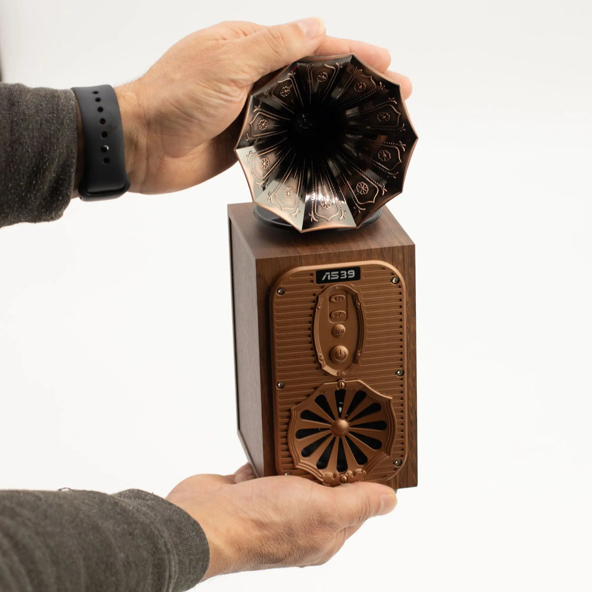Altavoz Bluetooth Ancient Wisdom retro con forma de gramófono en madera y bronce, sostenido por ambas manos.