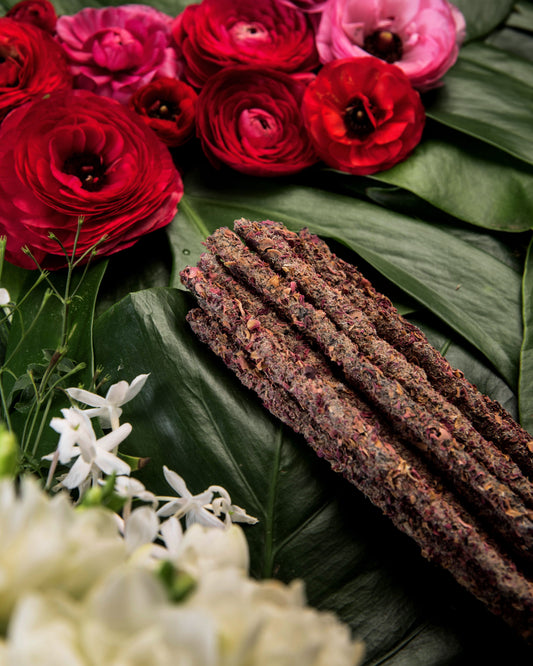 Incienso botánico de pétalos sobre hojas verdes, decorado con flores de jazmín blanco y rosas rojas frescas.
