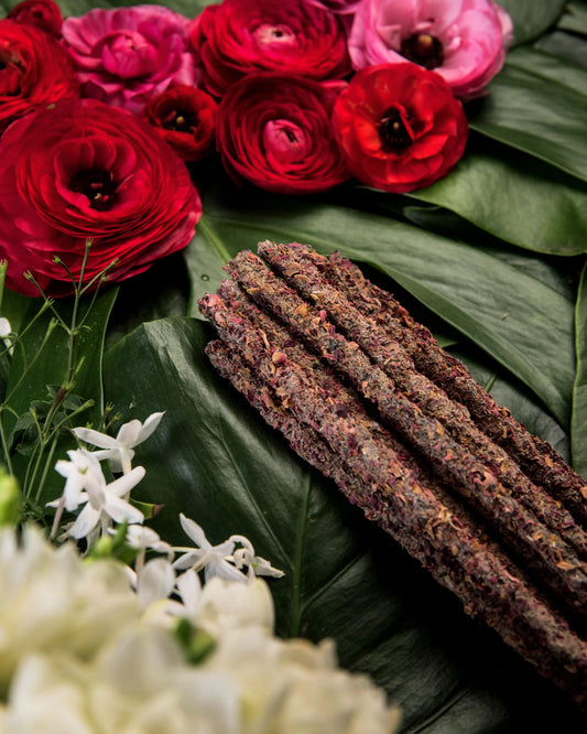 Incienso botánico de pétalos sobre hojas verdes, decorado con flores de jazmín blanco y rosas rojas frescas.