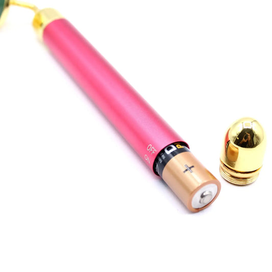 Rodillo facial de jade con mango rosa metálico, detalles dorados y compartimento abierto para pila, sobre fondo blanco.