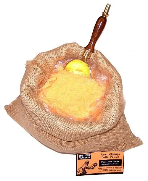 Saco de arpillera con sales de baño amarillas, cuchara de madera y etiqueta Ancient Wisdom, sobre fondo blanco.