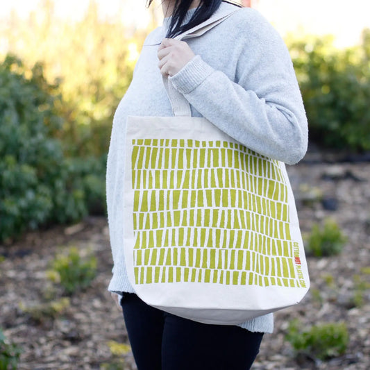 Bolsa de algodón natural colgada al hombro con estampado de rectángulos verticales en color verde oliva.