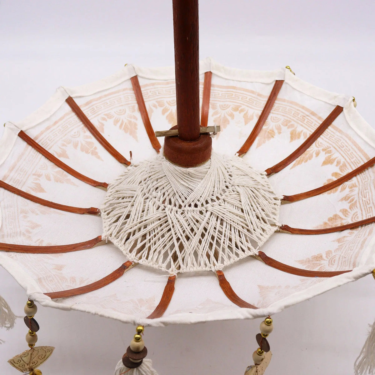 Sombrilla artesanal de Bali con lona blanca, detalles dorados, estructura de madera y tejido de macramé en el centro.