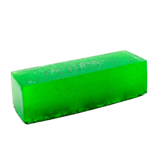 Barra de jabón artesanal rectangular, color verde translúcido con incrustaciones de semillas oscuras, fondo blanco.