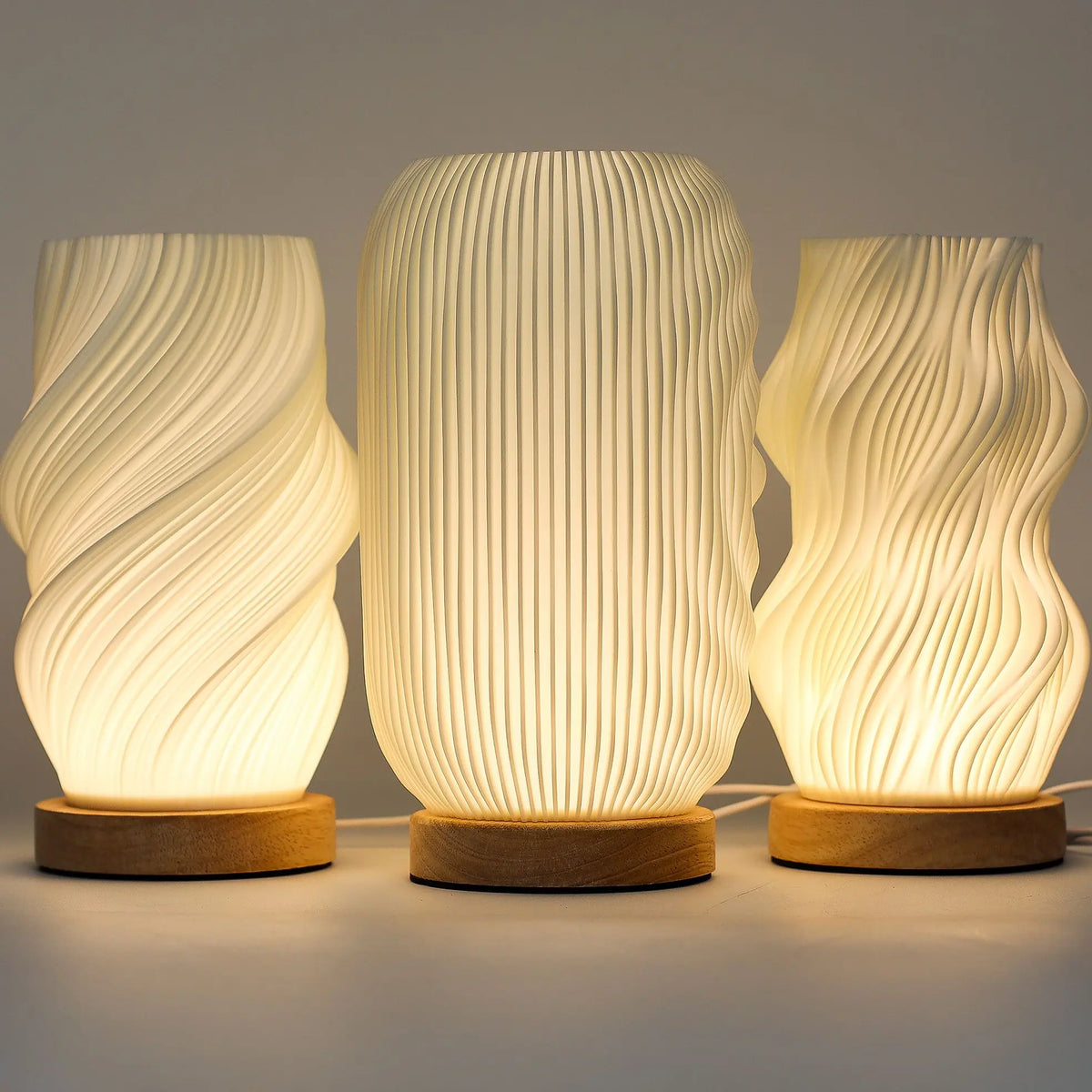 Tres lámparas LED modernas de diseño estriado y orgánico sobre bases de madera clara, con luz cálida difusa.