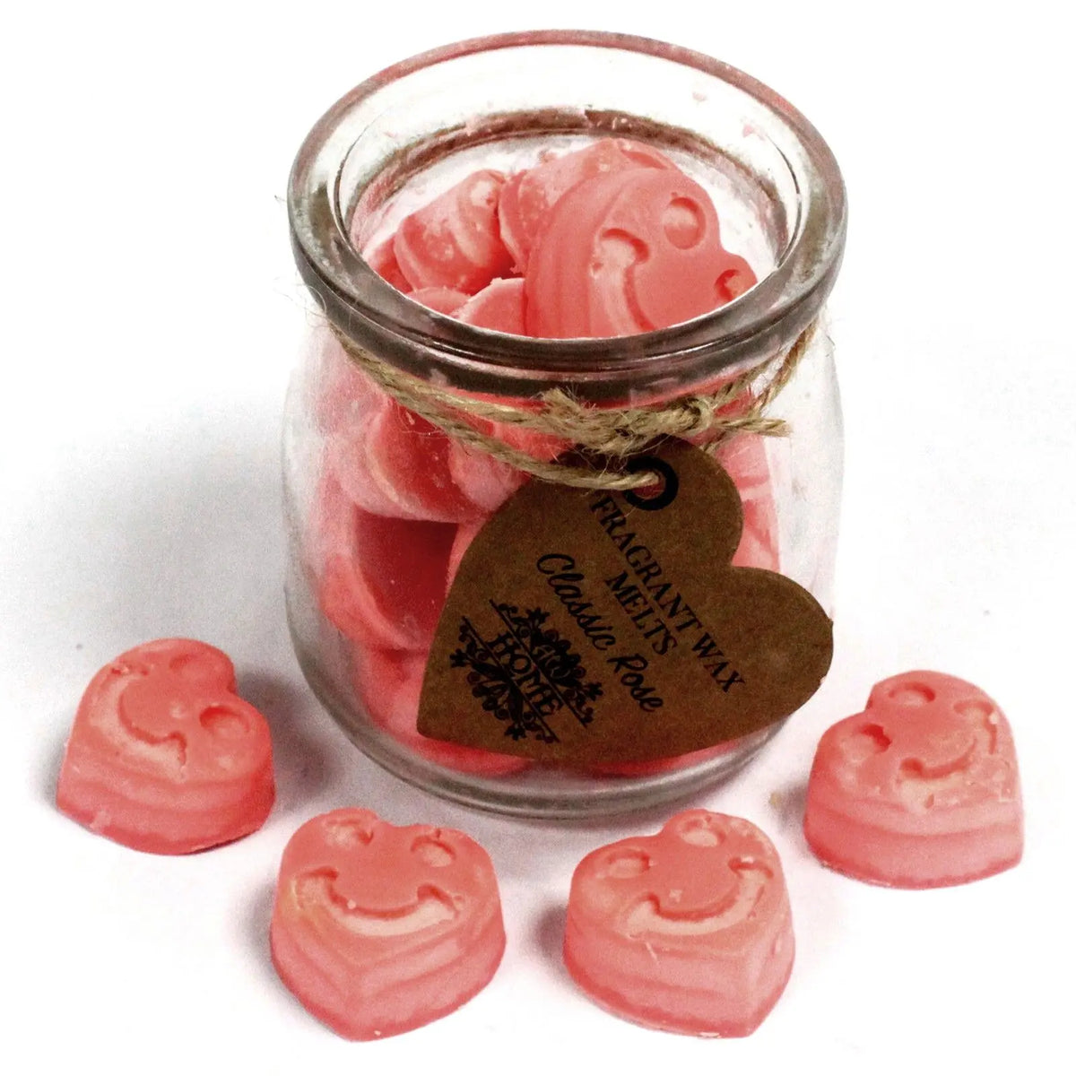 Frasco de vidrio con figuras de cera de soja rosa en forma de corazón con carita feliz sobre fondo blanco.
