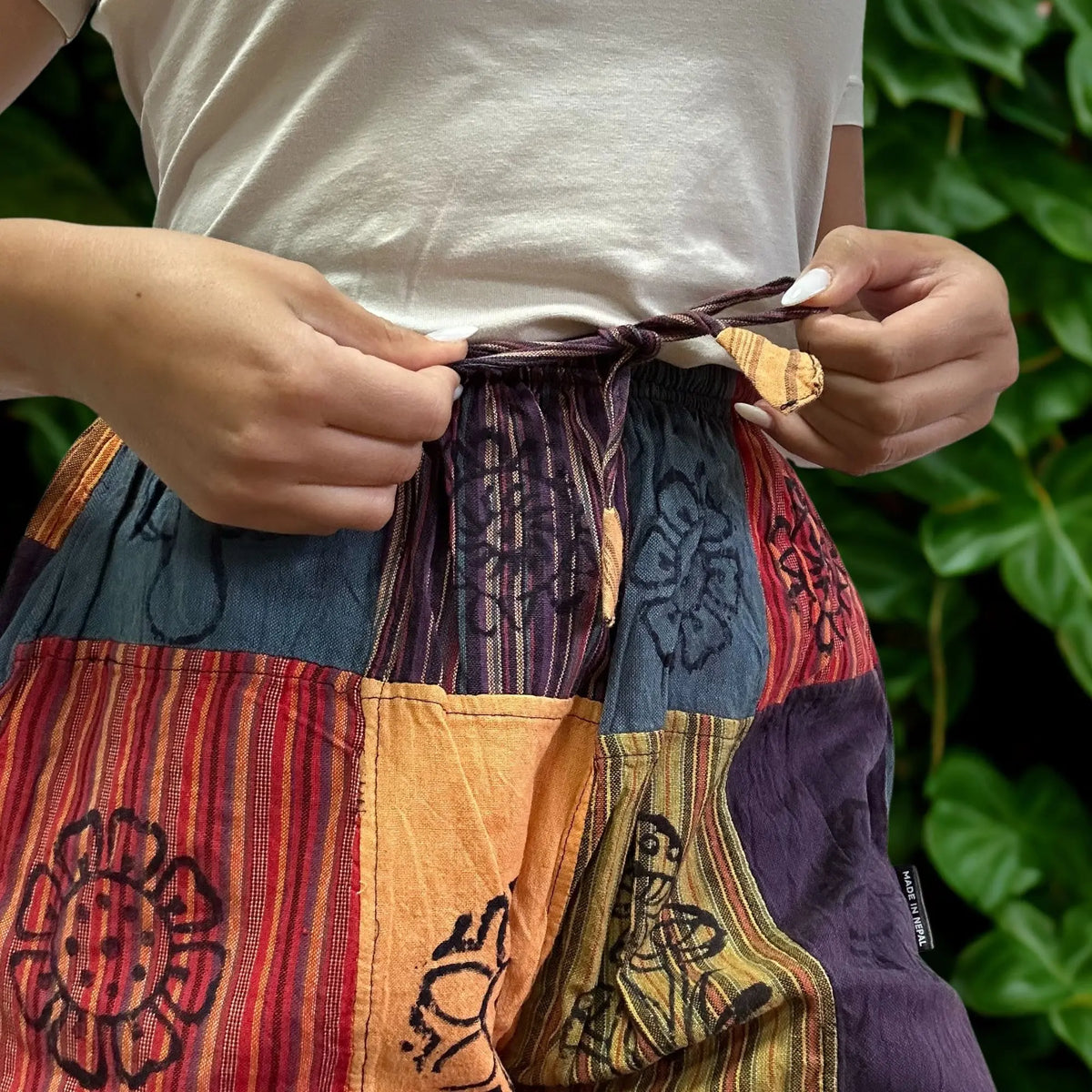 Pantalón estilo nómada de parches con estampados florales y de hongos en tonos naranja, morado y azul con cordón.