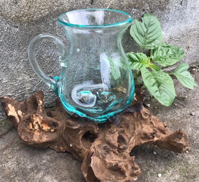 Jarra de vidrio fundido transparente con tinte azul sobre una base de madera natural, estilo artesanal y orgánico.