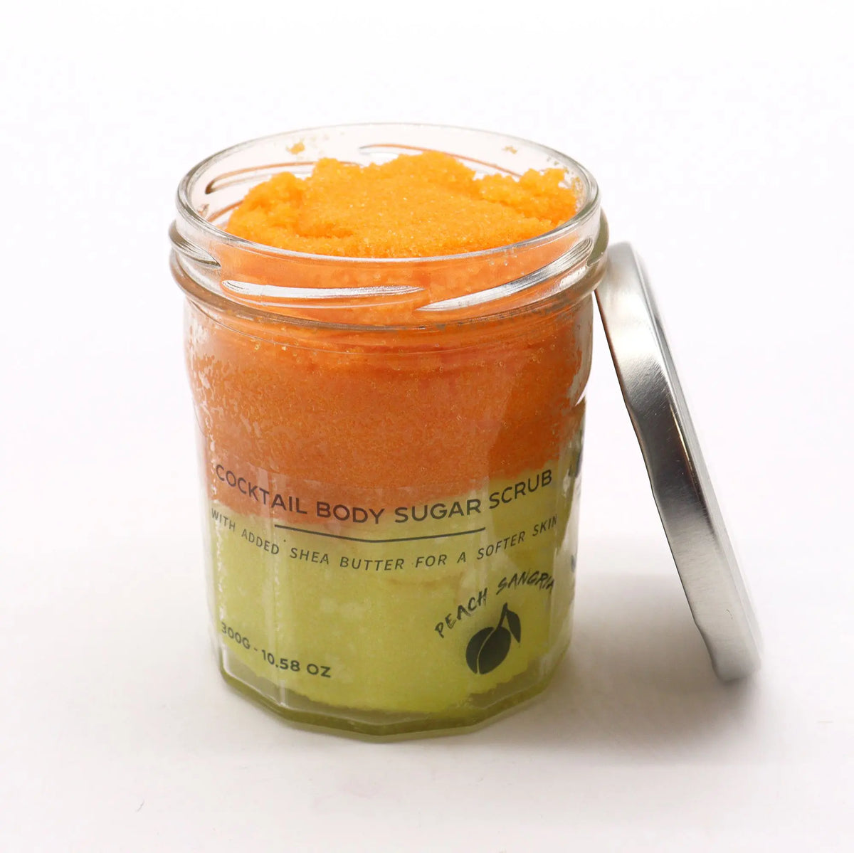 Frasco de vidrio con exfoliante de azúcar en capas naranja y amarilla, tapa metálica a un lado, fondo blanco.