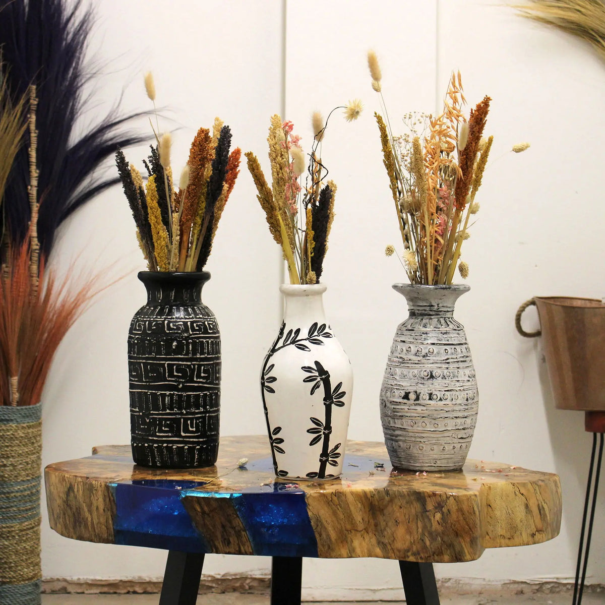 Tres jarrones de cerámica decorativos con flores secas sobre una mesa de madera y resina azul estilo artesanal rustico